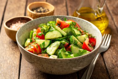 Salatalıklı taze sebze salatası, domates ve sebzeler kırsal ahşap masada kasede. Seçici odak.