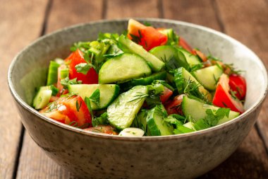 Salatalıklı taze sebze salatası, domates ve sebzeler kırsal ahşap masada kasede. Seçici odak.