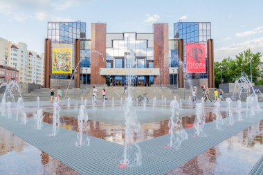 Saratov / Russia - June 21, 2017: The modern building of the Saratov academic theater of the young spectator. Urban planar fountain. Summer day. People walk on the street. clipart