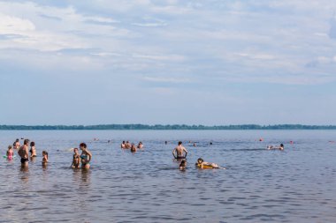 İnsanlar sahilde nehirde yüzmek. Güneşli yaz günü. Pitoresk bulutlar gökyüzünde. Nehir manzara.