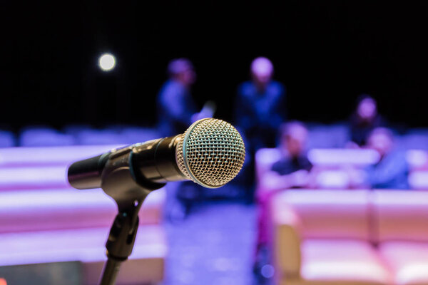 Wireless microphone on the stand. Blurred background. People in the audience. Show on stage in the theater or concert hall.