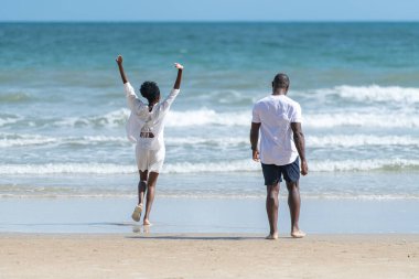 Happy couple enjoying a playful walk on the beach, laughing and holding hands as they splash through the waves together