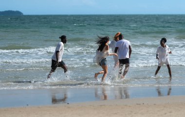 Group of diverse friends having fun at the beach, running and splashing in the waves on a sunny day