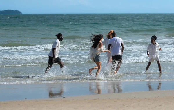 Group of diverse friends having fun at the beach, running and splashing in the waves on a sunny day