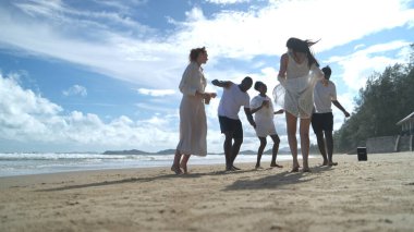 Group of diverse friends having fun at the beach, drink and dance in the waves on a sunny day
