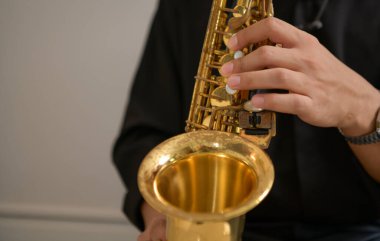 Kapalı bir odada, yumuşak ışıklandırmalı saksafon çalan genç bir Asyalı. Ev müziği stüdyosunda rahat bir solo performans.