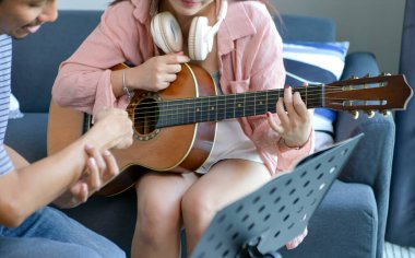 Genç Asyalı bir kadın gitar derslerinden zevk alırken bir erkek kararlılıkla ders veriyor. Yaratıcı, rahat stüdyo ortamında müzik pratiği yapıyor.