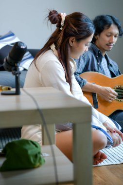 Erkek gitar ve mızıka çalarken mutlu Asyalı kadın kulaklıkla müzik dinliyor. Doğal ışıklandırmada rahat müzik oturumu