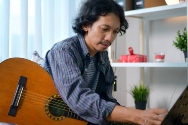 Genç Asyalı adam evde gitarla müzik yapıyor. Yaratıcı, rahat stüdyo ortamında müzik pratiği yapıyor.
