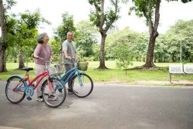 Parkta bisiklete binen mutlu Asyalı çift dışarıda güzel vakit geçiriyorlar, huzurlu bir günde konuşup gülümsüyorlar.