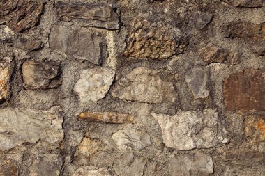Doğal taşlar beton harca gömülüdür. Detaylı yüzeylere sahip taş bir duvarın kabataslak desenli yakın plan görüntüsünü oluştururlar..