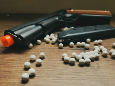 A black airsoft gun with several white BBs. Though just a replica, the photo showcases the weapon's beauty while evoking power and danger.