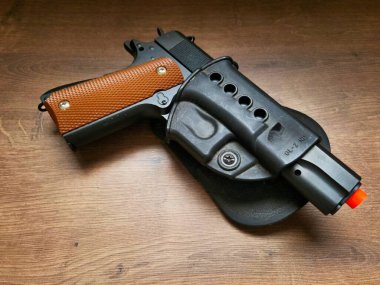 Turuncu saplı modern bir tabanca. Havadan kopyasına rağmen, fotoğraf silahın güzelliğini sergiliyor, bir güç ve tehlike hissi uyandırıyor..