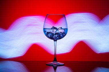 Mavi ışıklar bir kırmızı zemin üzerine içki ve buz küpleri ile bir bardak.