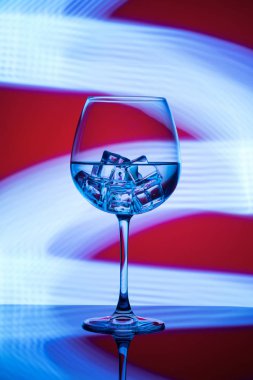 Mavi ışıklar bir kırmızı zemin üzerine içki ve buz küpleri ile bir bardak.