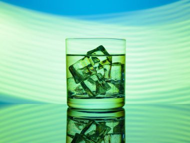 Bir bardak yeşil ışıklar ile mavi bir arka plan bir içki ve buz küpleri ile.