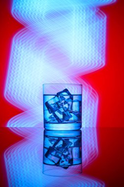 Mavi ışıklar bir kırmızı zemin üzerine içki ve buz küpleri ile bir bardak.