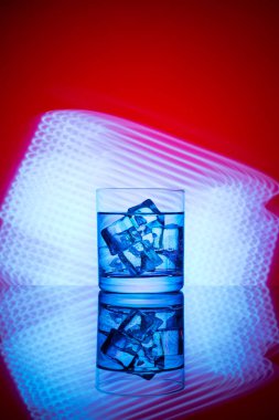 Mavi ışıklar bir kırmızı zemin üzerine içki ve buz küpleri ile bir bardak.