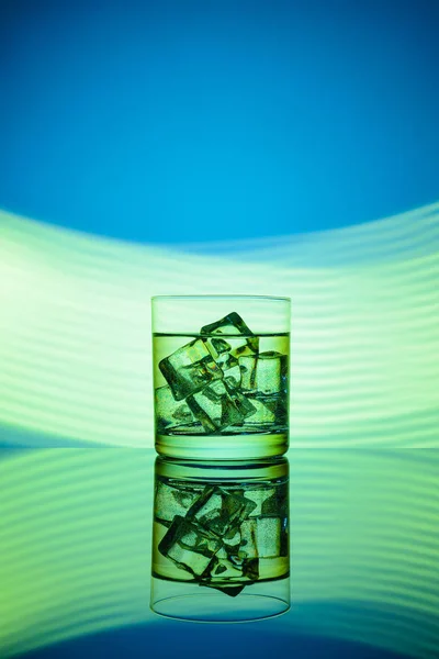 グリーン ライトと青色の背景に飲み物やアイス キューブとガラス — ストック写真