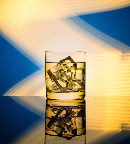 Altın ışık ile mavi bir arka plan bir içki ve buz küpleri ile bir bardak.