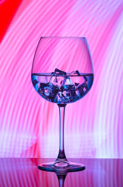 Mavi ışıklar bir kırmızı zemin üzerine içki ve buz küpleri ile bir bardak.