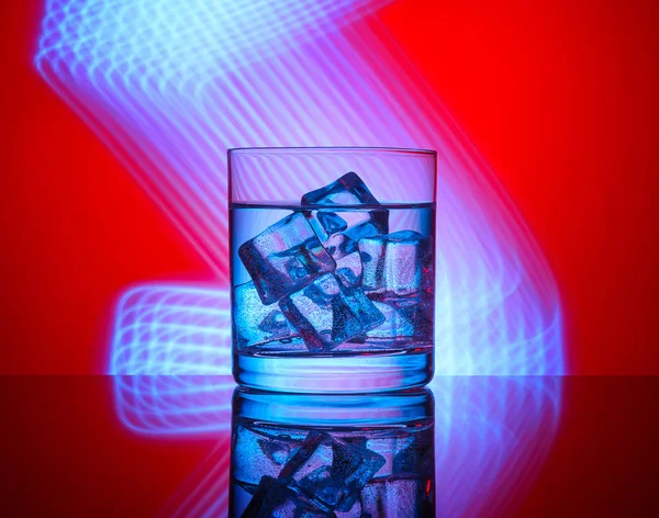 Mavi ışıklar bir kırmızı zemin üzerine içki ve buz küpleri ile bir bardak.