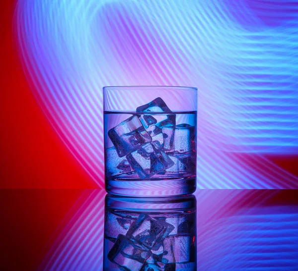 Mavi ışıklar bir kırmızı zemin üzerine içki ve buz küpleri ile bir bardak.