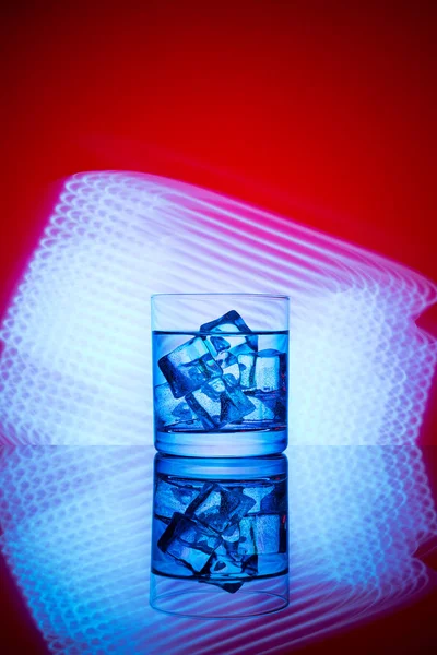 Mavi ışıklar bir kırmızı zemin üzerine içki ve buz küpleri ile bir bardak.