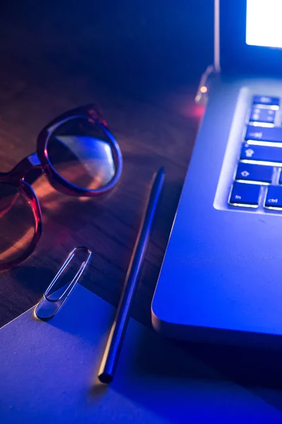 Notebook, pencil, glasses and computer in red and blue light.