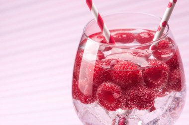 Saydam bir cam tüp pembe bir arka plan üzerinde bir kokteyl ile ahududu içki.