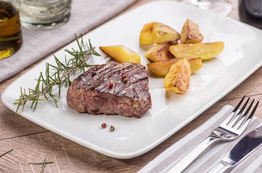 Sığır eti biftek ile kızarmış patates dilimleri bir restoranda bir beyaz dikdörtgen plaka üzerinde.