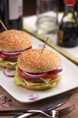 Hamburger çift peynir, kırmızı soğan ve domates beyaz dikdörtgen plaka restoran parlak bir tablo ile.