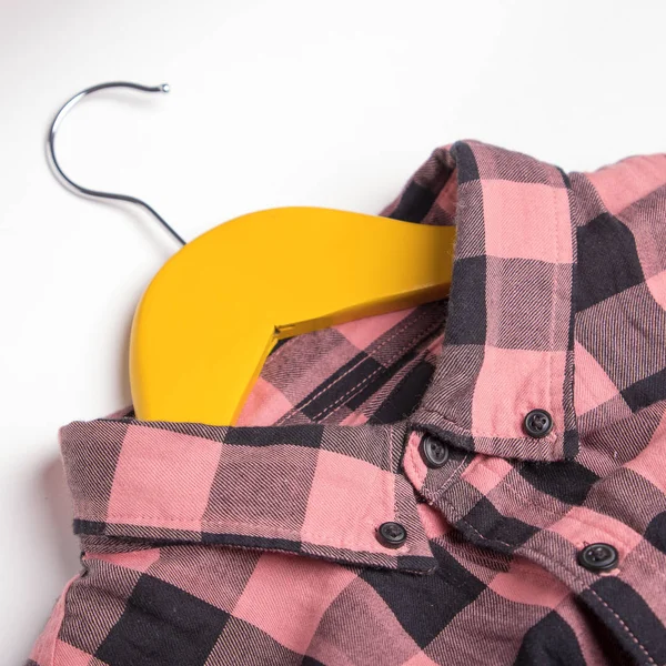 Plaid pink shirt on yellow hangers on a white background.