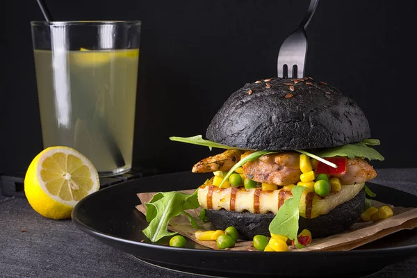 Chicken hamburger in a black bun with lemonade on a black plate.