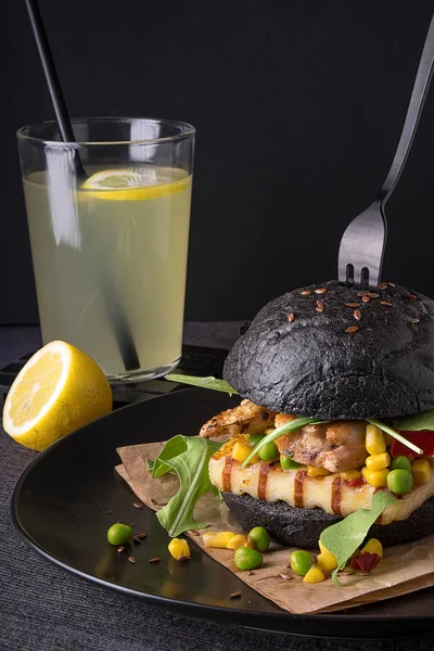 Chicken hamburger in a black bun with lemonade on a black plate.