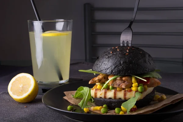 Chicken hamburger in a black bun with lemonade on a black plate.