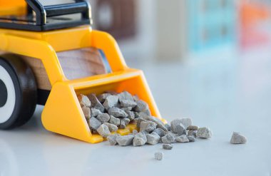 Sarı bir oyuncak buldozer, mavi pencereli bir evin arka planına karşılık metal para topluyor..