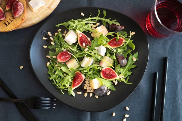 Koyu gri masa örtüsünde siyah tabakta Camembert ve incir salatası..