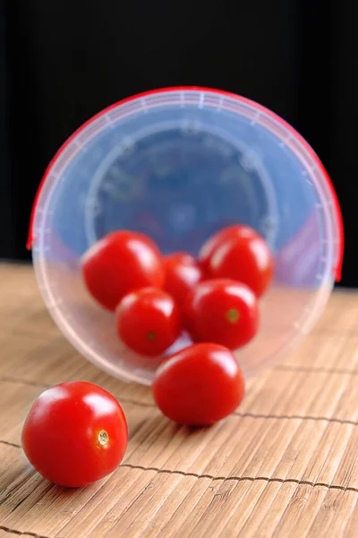 Ahşap ve siyah arka planda plastik kovada kiraz domatesleri.