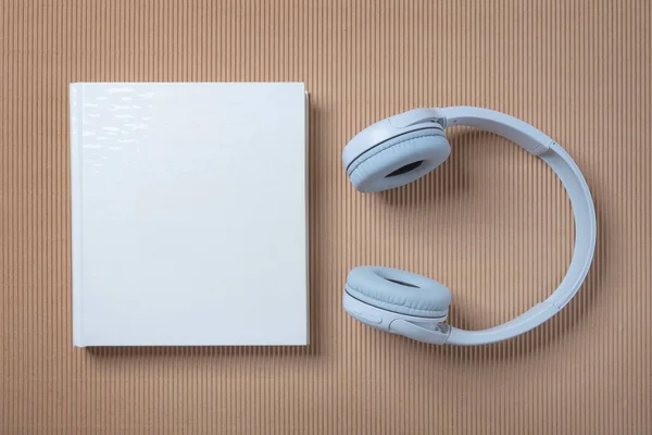 Λευκά Ακουστικά Και Ένα Λευκό Βιβλίο Για Μπλε Και Μπεζ — Φωτογραφία Αρχείου