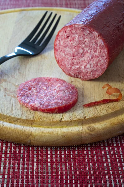 A slice of salami sausage on a black fork on a wooden board. Beautiful blurred background.