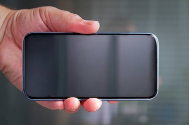 Elinde cep telefonu olan pembe ekose gömlekli bir adam. Beyaz tişört.