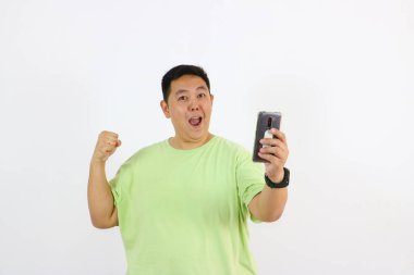 Elinde telefon tutarken heyecanlı bir ifadeyle genç bir adamın portresi evet başarısı jesti yapıyor.