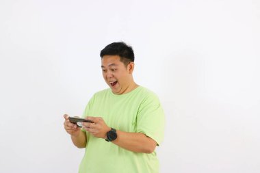 Genç Asyalı bir adamın yüzü telefonu sımsıkı tutarken saf mutluluk ve neşe gösteriyor.