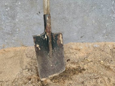 Paslı kürek, duvarın yanındaki kumda duruyor. Bahçıvanlığı ve sıkı çalışmayı simgeliyor.