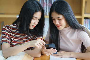 Genç Asyalı kadın öğrenci eğitimi alıyor ve libr 'deki kitapla not alıyor.