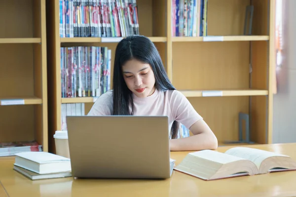 Young Asian woman student study and take notes with book in libr