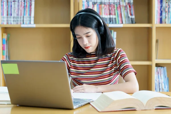 Young Asian woman student study and take notes with book in libr