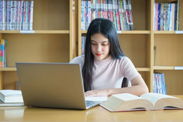 Een vrouwelijke universiteitsstudent aan tafel die opdrachten doet in de universiteitsbibliotheek. Een student gebruikt de laptop en leert online. — Stockfoto