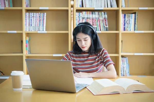 Een vrouwelijke universiteitsstudent aan tafel die opdrachten doet in de universiteitsbibliotheek. Een student gebruikt de laptop en leert online. — Stockfoto